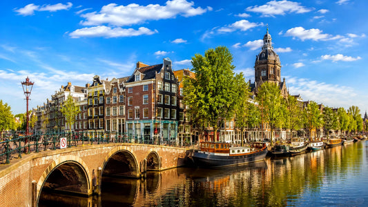 breedbeeldfoto van een historische Amsterdamse gracht met karakteristieke brug, woonboten en grachtenpanden in Amsterdam, Nederland – sfeervolle landmarkfoto voor meubels herstofferen en meubelstoffering in Amsterdam