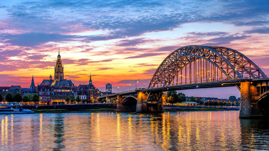 Breedbeeldfoto van de iconische Waalbrug en historische skyline van Nijmegen, Nederland, met uitzicht over de rivier bij zonsondergang – professionele 8K landmarkfoto voor meubels herstofferen en meubelstoffering in Nijmegen.